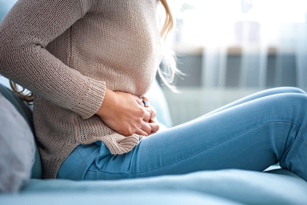 Woman sitting on a sofa holding her lower abdomen with both hands